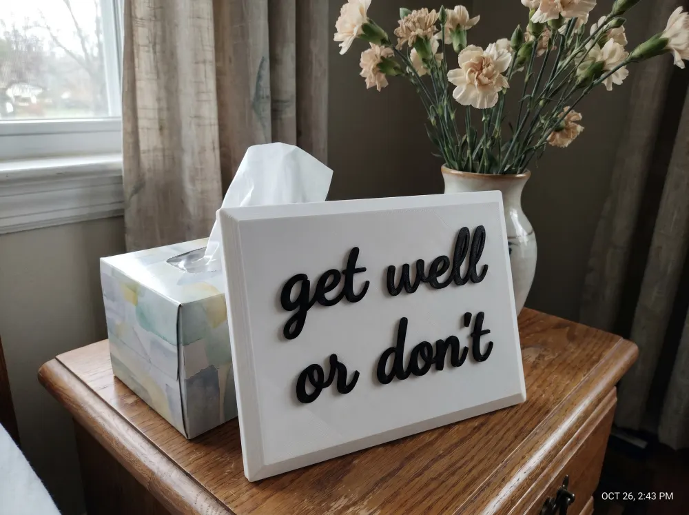 A 3D-printed Thudletter slab with raised handwritten lettering reading 'get well or don't', shown in a real home setting.