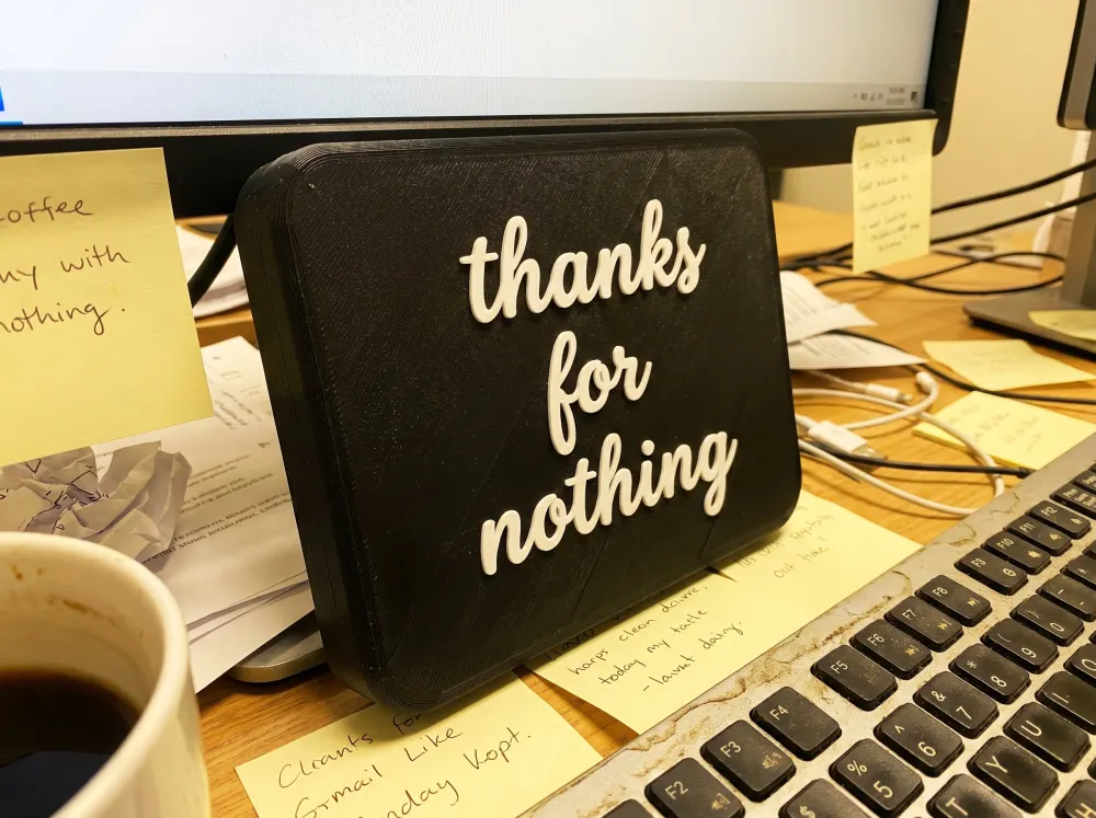 A 3D-printed Thudletter slab with raised handwritten lettering reading 'thanks for nothing', shown in a real home setting.