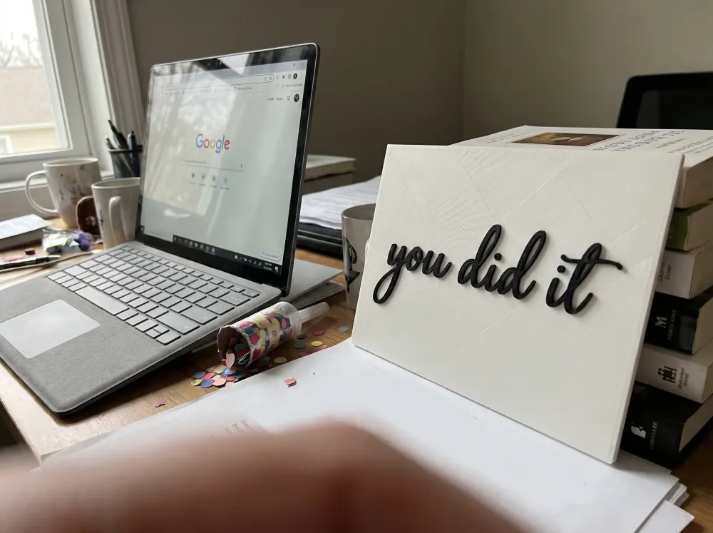 A 3D-printed Thudletter slab with raised handwritten lettering reading 'you did it', shown in a real home setting.