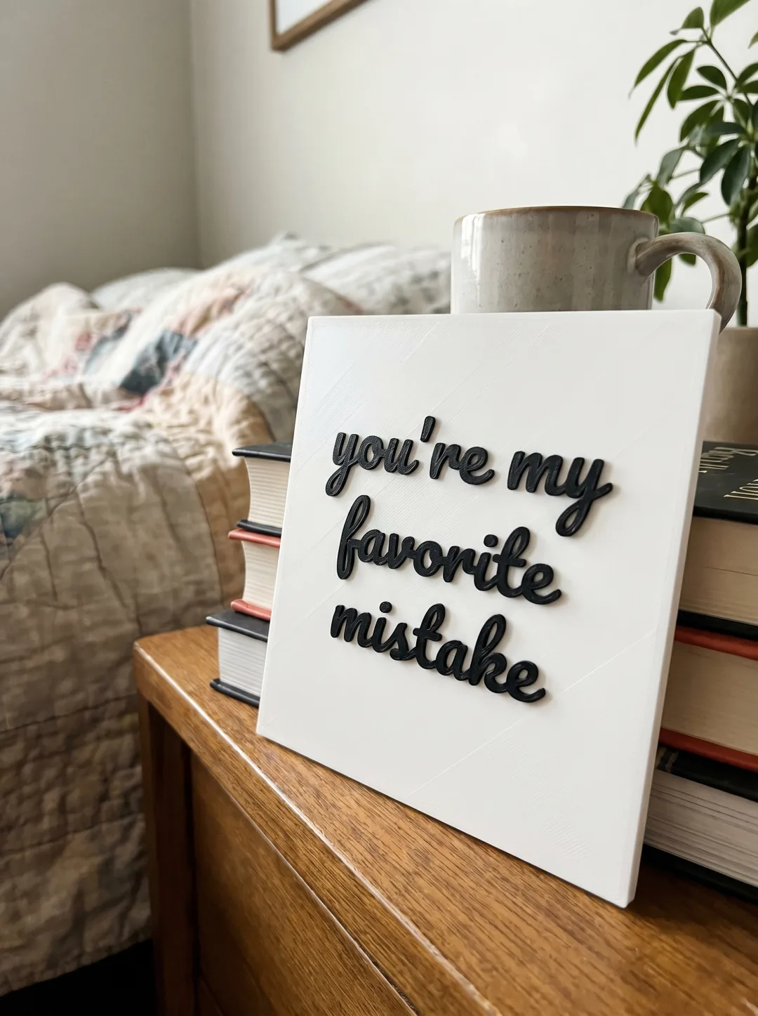 A 3D-printed plastic slab on a nightstand with raised handwritten lettering reading 'you're my favorite mistake'.